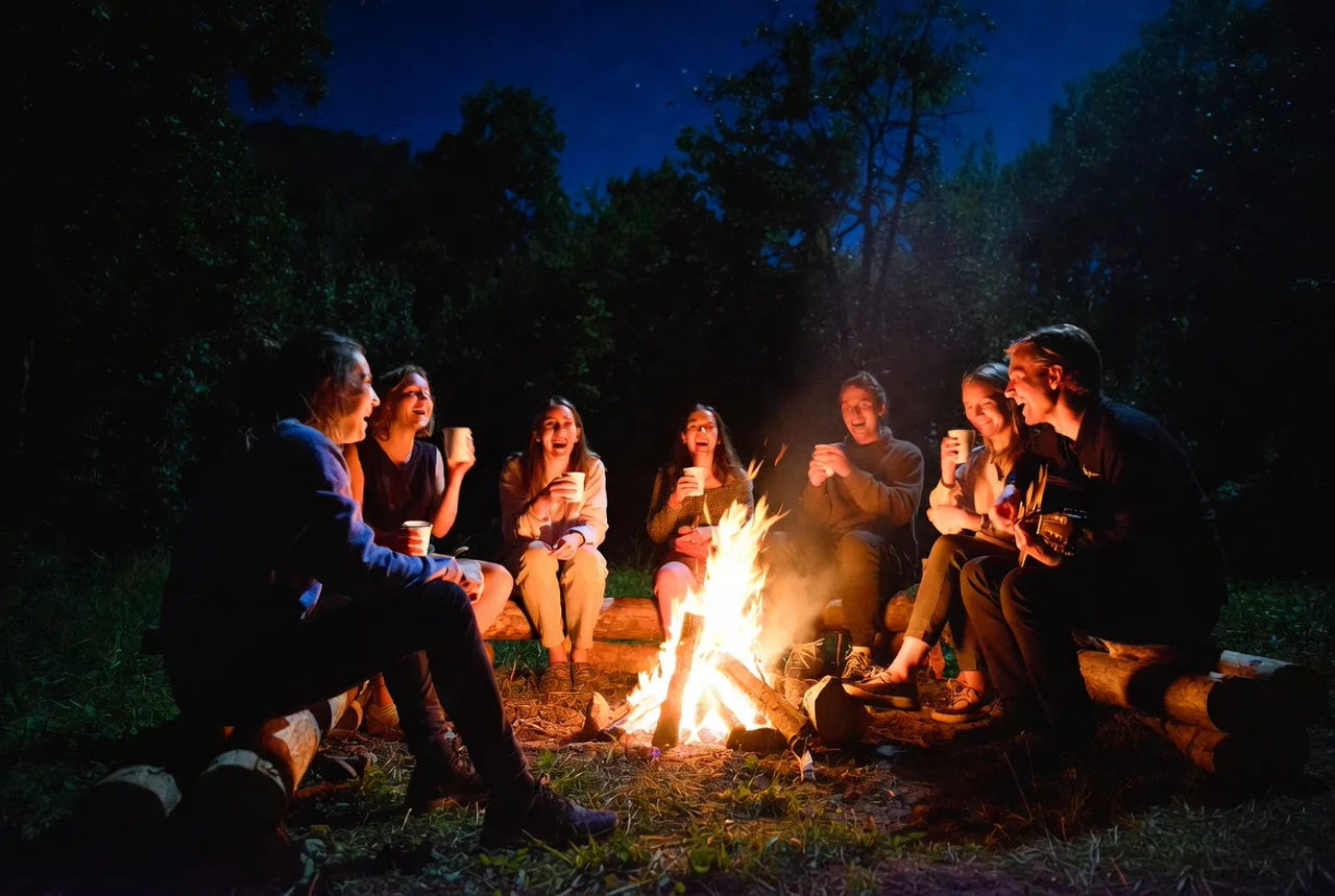 Glückliche Gruppe sitzt abends am Lagerfeuer und singt während eines Camping-Retreats